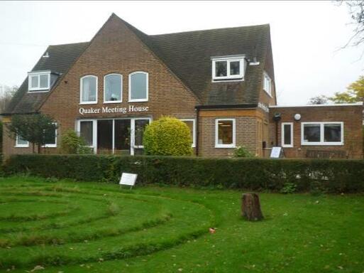 Enlarge simple building entirely faced in red brick with a white sign on top of main entrance 'Quaker Meeting House'.