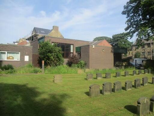 Brick flat roofed building sits next to a burial ground. 