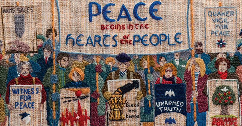 colourful panel of tapestry says Peace begins in the hearts of the people includes dozen figures with placards