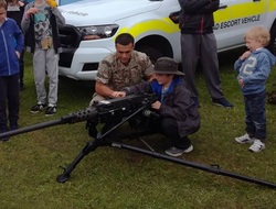 A child is shown a machine gun by soldiers. 
