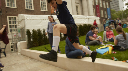 child jumping in the air. People sitting on grass chatting.