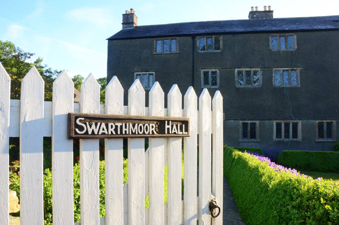 Gate with a sign saying 'Swarthmoor Hall' on it. Gate leads to a large old house.