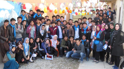 A group of Afghan peace volunteers in a courtyard with balloons. Several are making the peace sign 'v' with their fingers