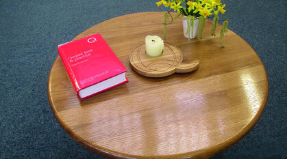 A picture of a wooden table with a handmade 'Q' candle holder, flowers, and Quaker Faith and Practice