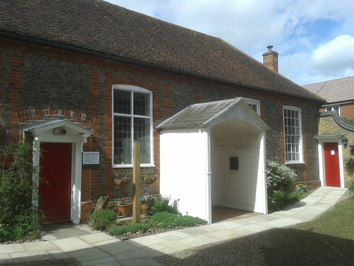 Grey and red brick building with long windows and wide white entrance porch.