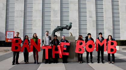 People standing in front of the statue outside the UN of a gun with its barrel tied in a knot, holding up letters spelling out 'ban the bomb'