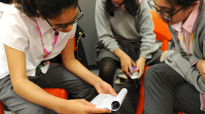 three girls sitting together talking over an exercise on a piece of paper