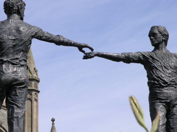 bronze sculpture of two figures reaching across a divide