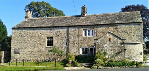 Large stone detached house with four small white-framed windows. 