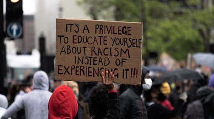 protestor holding a placard at a Black Lives Matter protest in London. Placard reads 'it is a privilege to educate yourself about racism instead of experiencing it'