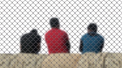 three men sat on concrete behind a chain link fence 