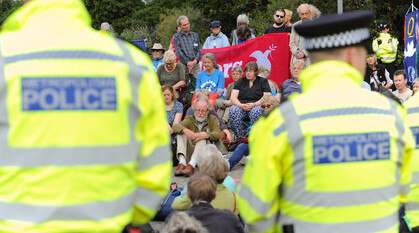 a quaker protest meeting for worship blocking the road to an arms fair. photo taken over the shoulder of two coppers