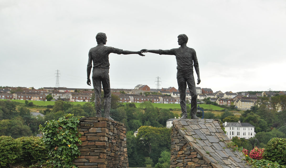 statue of men reaching out across a divide to shake hands