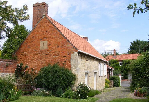 Small old stone cottage with low white doors and white-shuttered windows. 