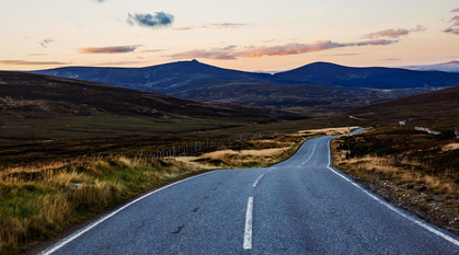 An empty road through the Scottish countryside. The road is clear ahead but winding.
