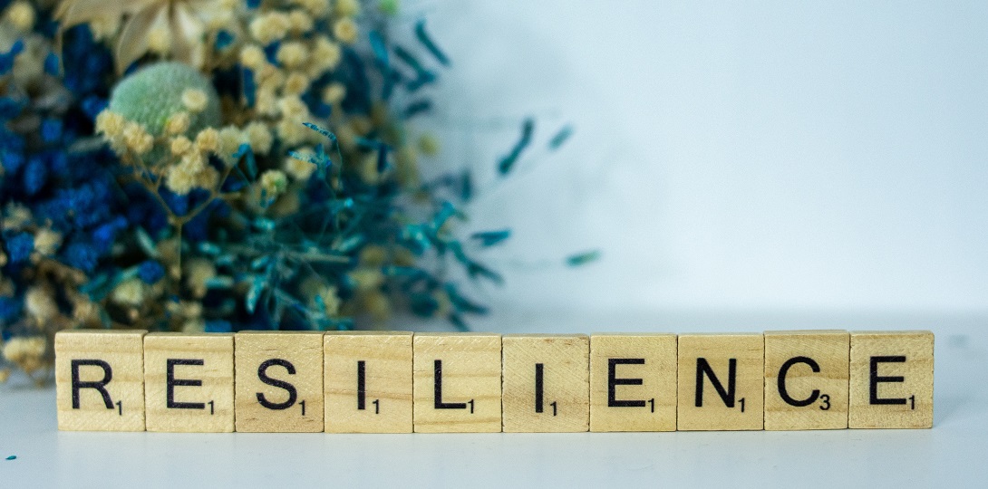 A photo of wooden scrabble tyles spelling out the word resilience with a bouquet of yellow flowers behind