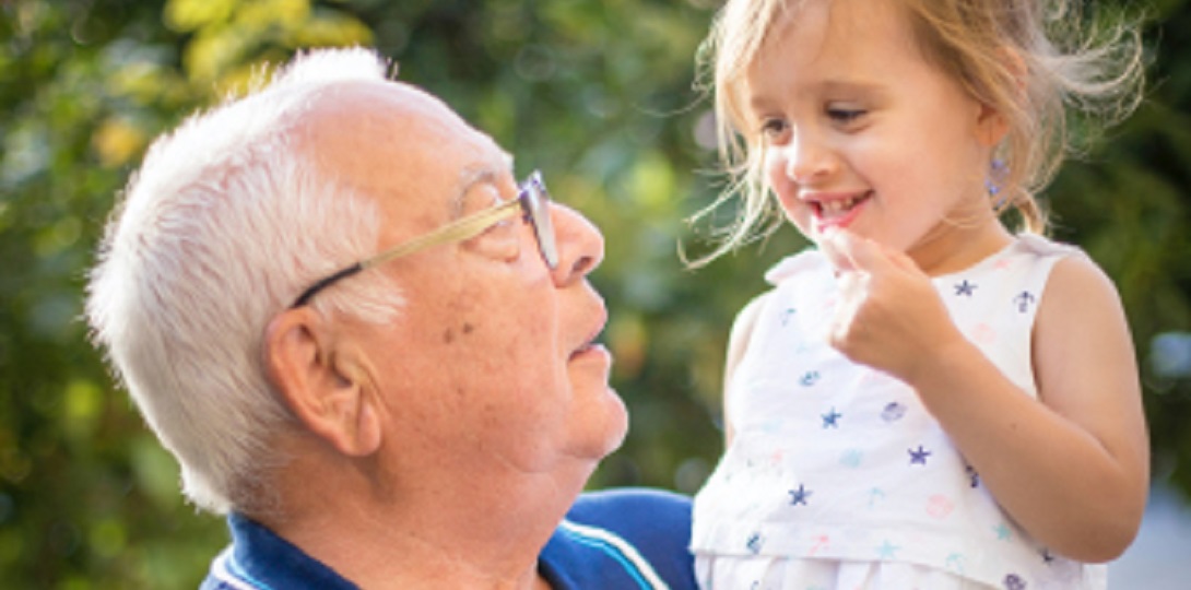 Elderly man in a blue shirt holding a little girl in a white dress in his arms