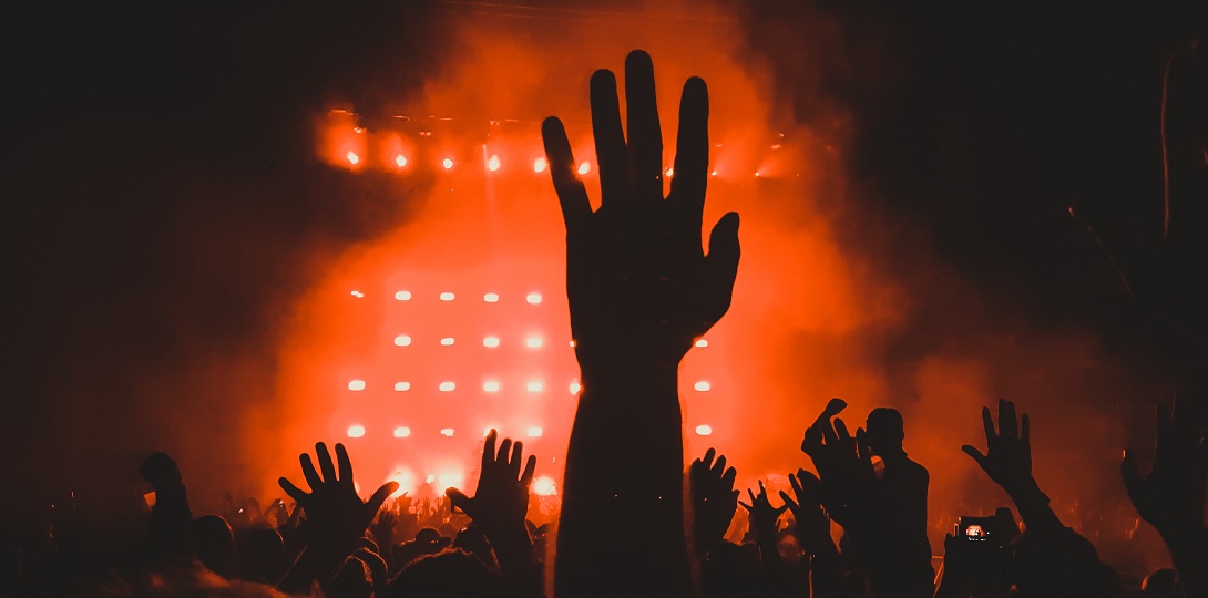 A dark room lit with orange lights and hands raised in the air.