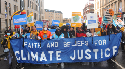 People marching behind a big banner saying 'faith and beliefs for climate justice'