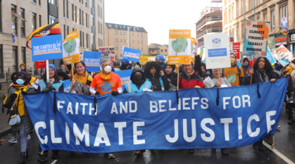 People marching behind a big banner saying 'faith and beliefs for climate justice'