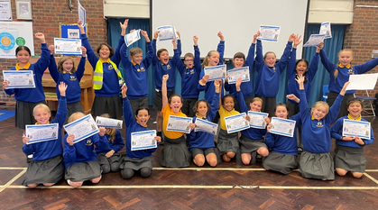 a classroom of primary school children posing for a photo in a school hall cheering with certificates