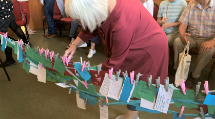 a person pegging a post-it note square to a string of other notes in a room full of people