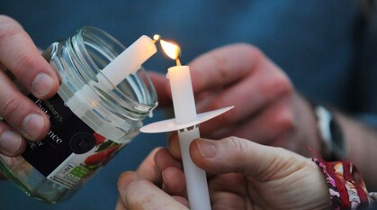 Close-up of hands holding a jar jar containing a candle lighting another candle held by another person