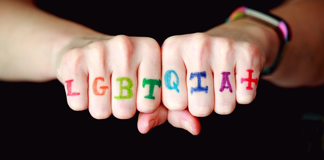 Two fists with the letters LGBTQIA+ painted across the fingers in rainbow colours