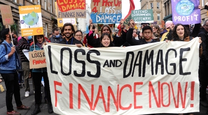 A group of people carrying a 'loss and damage finance now' banner at a march in Glasgow. Others people around are holding placards with signs about loss and damge finance, make polluters pay and climate justice.
