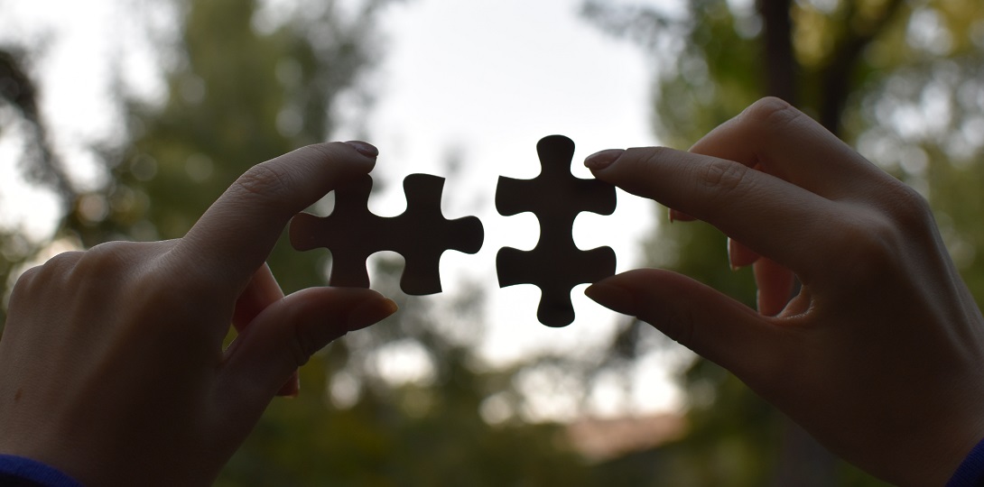 Black and white image of hands holding up two puzzle pieces