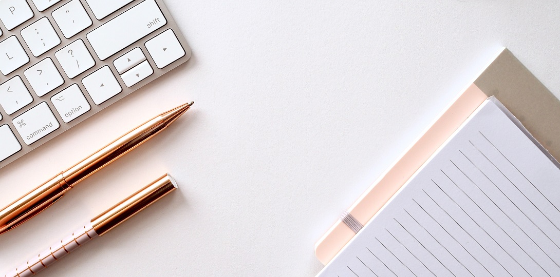 An image of a keyboard, pens and notebook