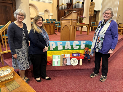 3 women surround a peace flag and various photos inside a church