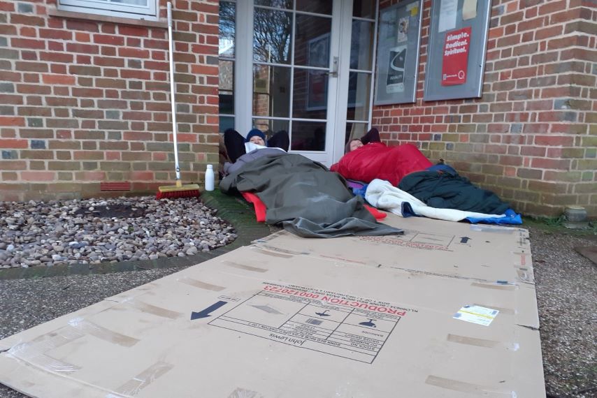 2 people lying down in a doorway on cardboard in sleeping bags.