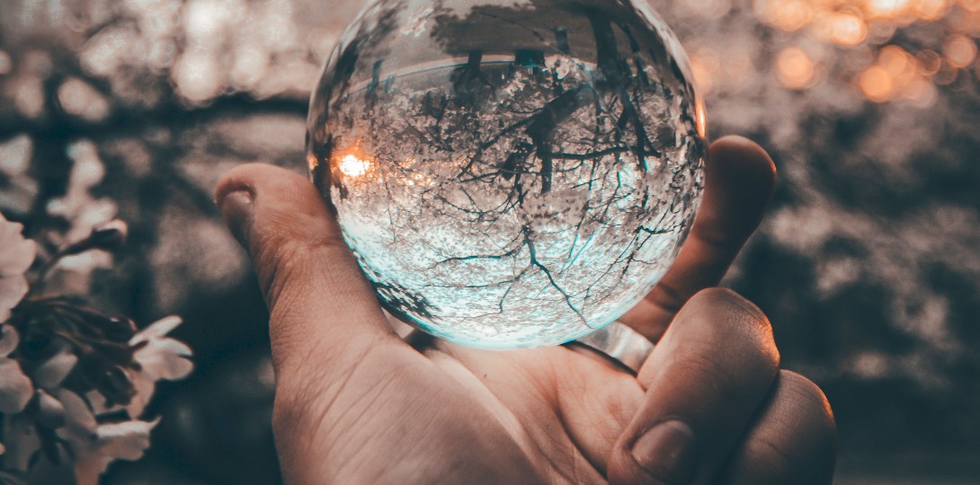 A hand holding a round crystal which is reflecting the countryside behind it.