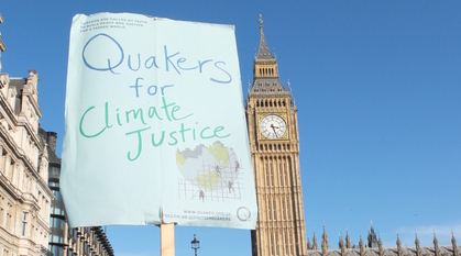 A Quakers for climate justice placard held up with Parliament in the background