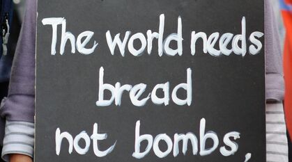 Close up of a placard around someone's neck saying "The world needs bread not bombs"