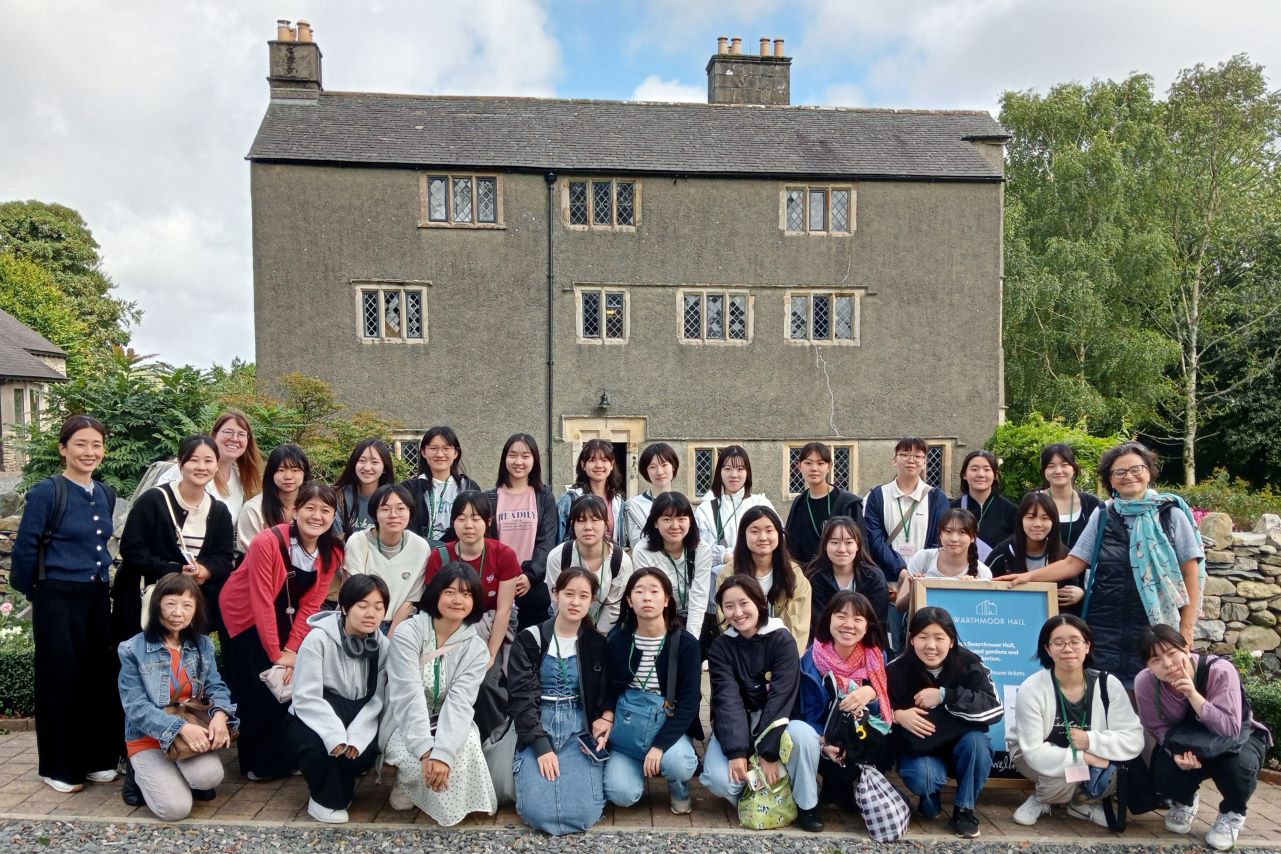 Group of students pose in front of large grey building