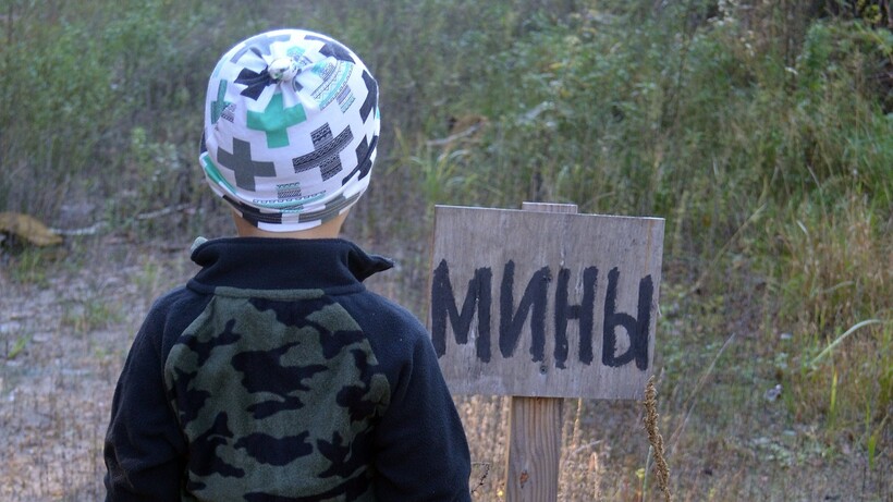 A child looks over a field with a sign warning of landmines. Photo: Sergey Kamshylin/Shutterstock.com