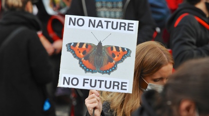 In the middle of a climate demonstration a woman holds up a placard with a small tortoiseshell butterfly on it and the words 'No Nature, No Future' around it