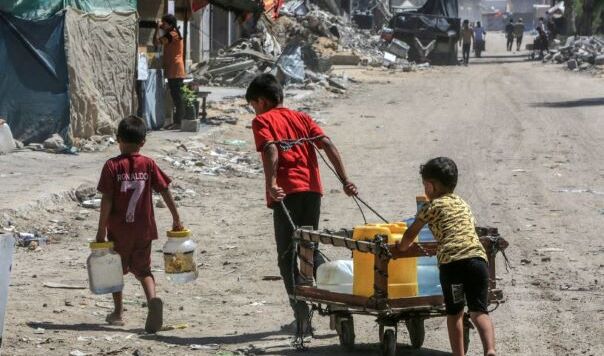 Young boys pulling water surrounded by ruined buildings