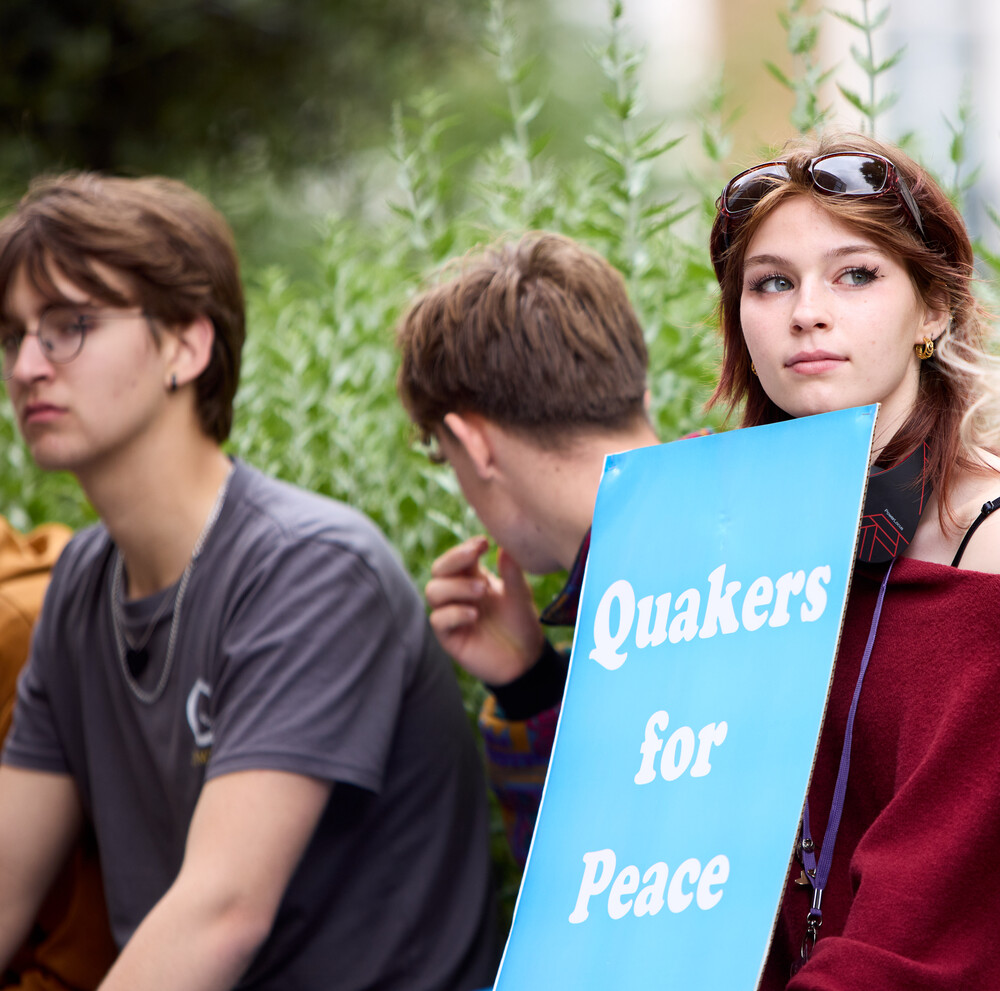 Three Friends sitting, one is holding a poster which says 'Quakers for Peace'