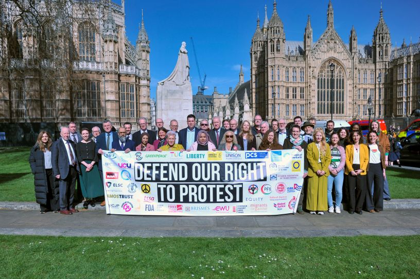 Large group of MPs and others behind banner near Houses of Parliament
