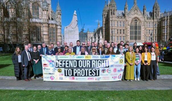 Large group of MPs and others behind banner near Houses of Parliament