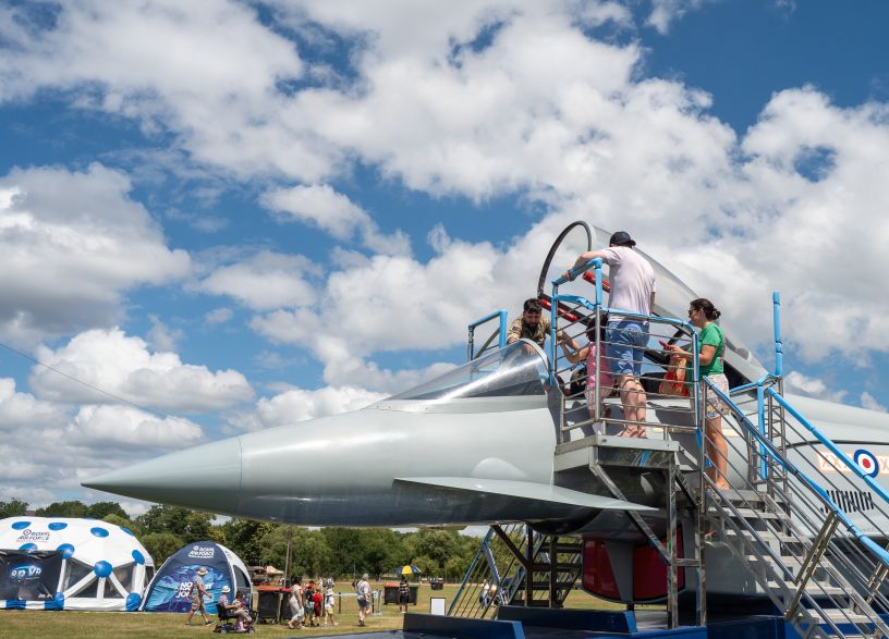 Grey fighter jet with civilians including a child looking in the cockpit