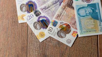 Two English £20 notes, one £10, and one £5 note on a wooden table
